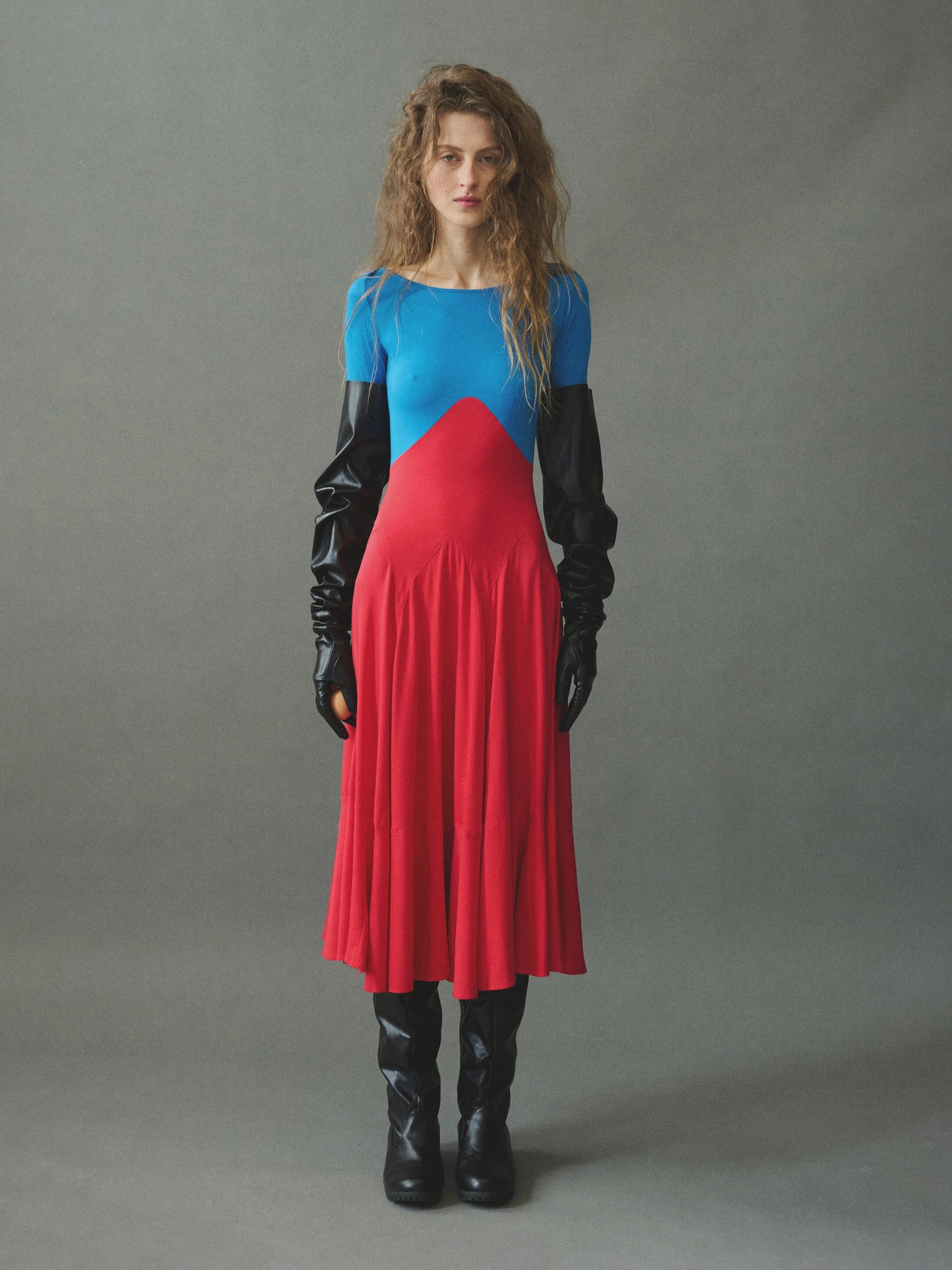 Model wearing red and blue color-block midi dress by EMILY DAWN LONG with a boat neckline, bracelet-length sleeves and full gathered skirt.