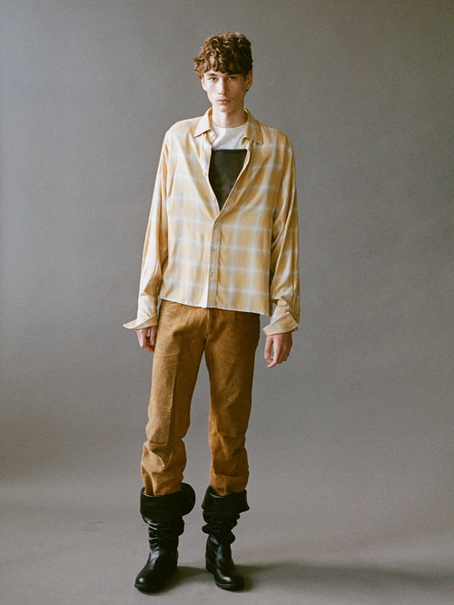 Person wearing a plaid shirt, brown pants, and black boots against a gray background