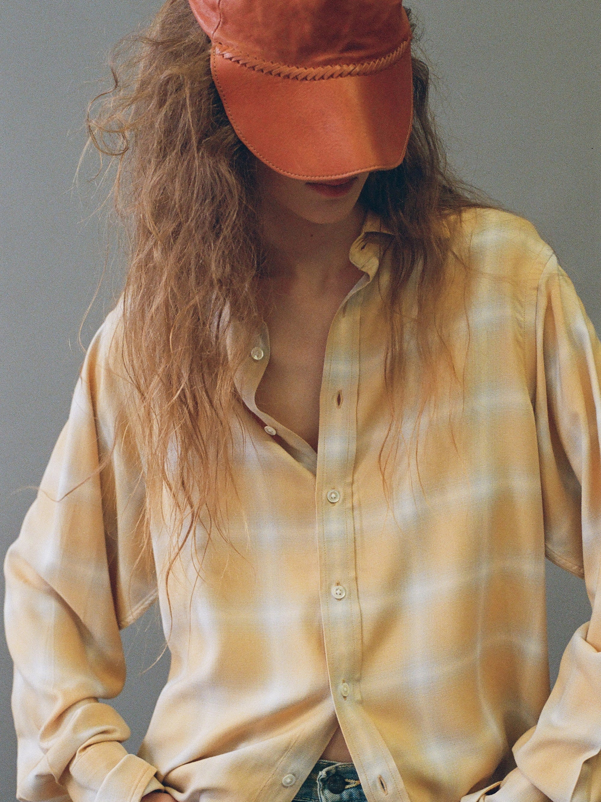 Person wearing a yellow plaid shirt and orange cap against a neutral background