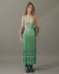Model wearing lily pad green pleated midi dress by EMILY DAWN LONG with an open back, fine shoulder straps and striped pleated skirt.