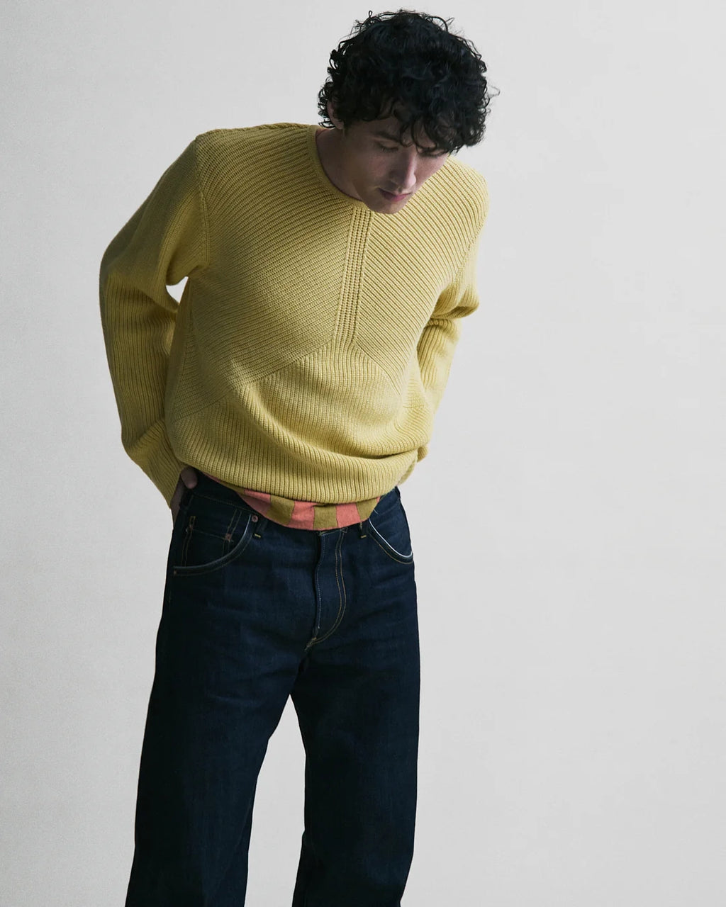 Person wearing a yellow sweater and dark jeans against a plain background
