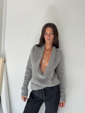 Woman wearing a gray sweater against a white wall