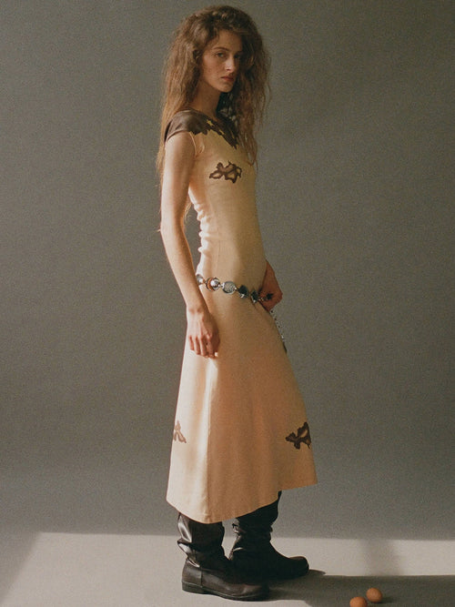 Woman wearing a beige dress with black patterns on a plain background