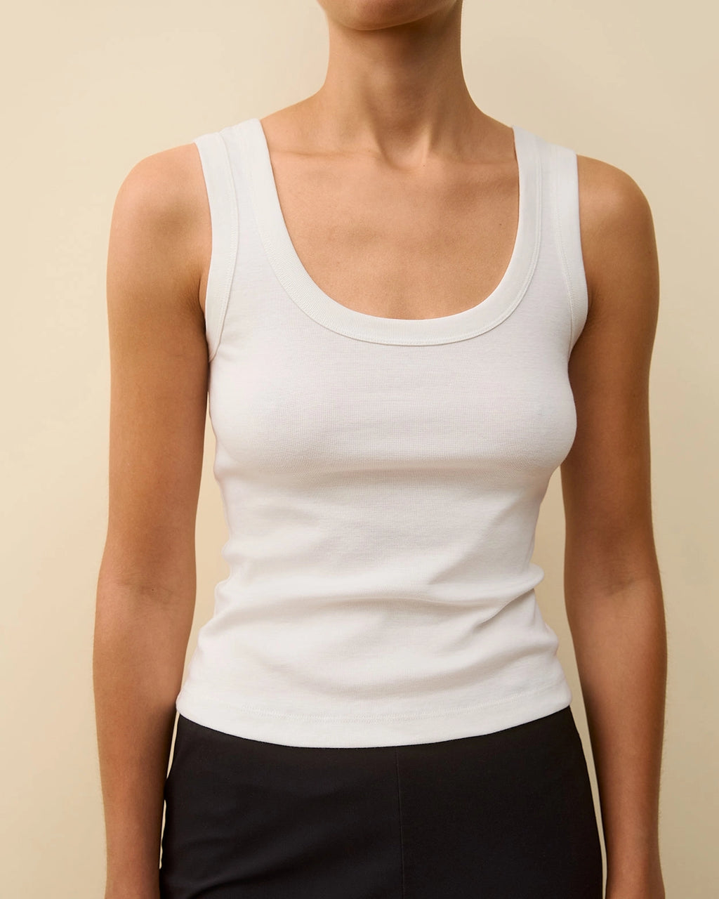 Model wearing the Hillie Tank in White by FLORE FLORE, a fitted tank in organic cotton jersey with a scoop neckline.