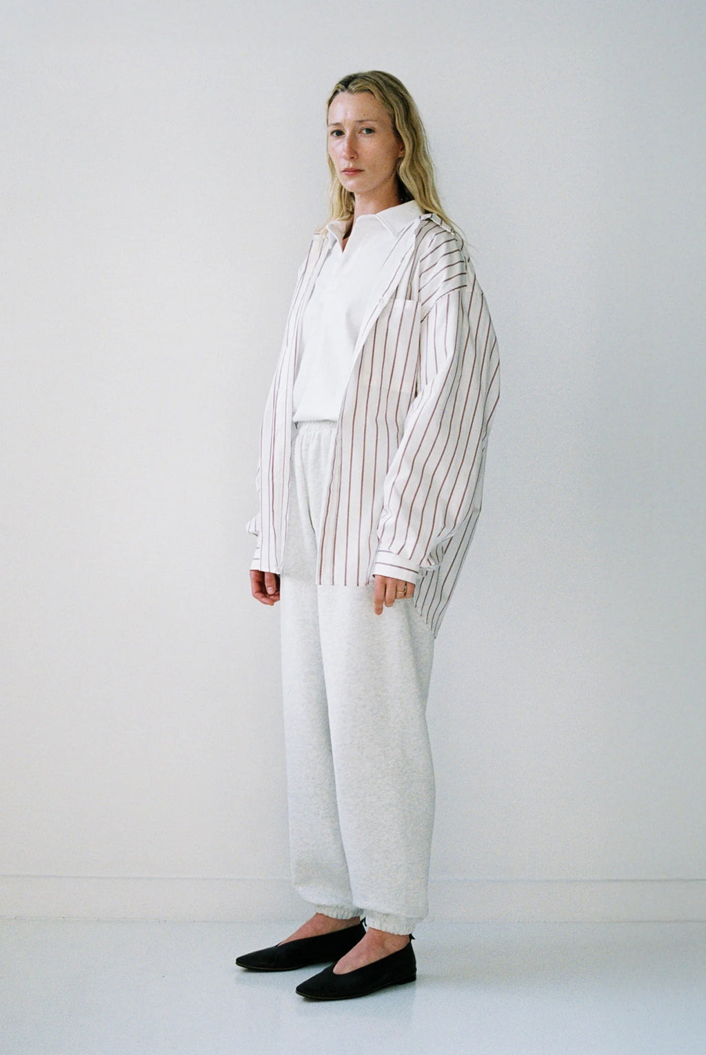 Woman wearing a white shirt, striped blazer, and white pants against a plain background