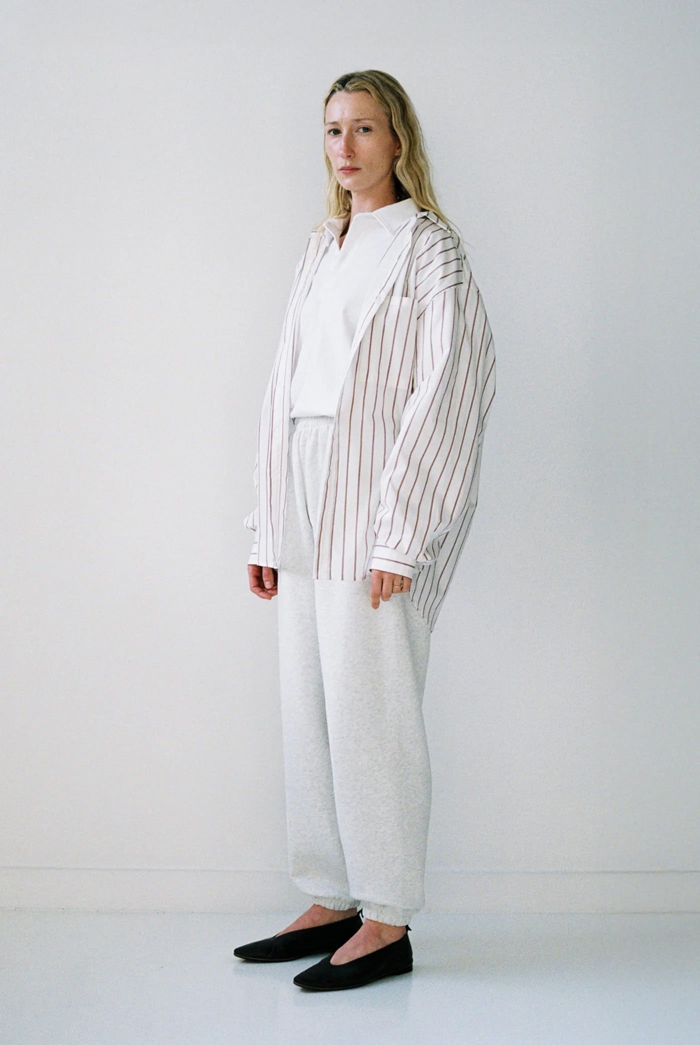 Woman wearing a white shirt, striped blazer, and white pants against a plain background