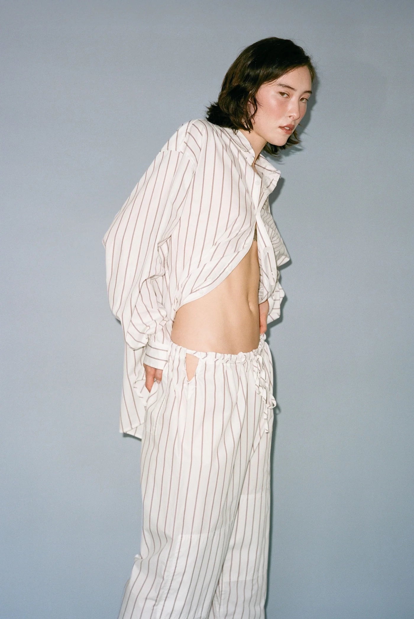 Person wearing a loose-fitting, off-white striped shirt and pants against a plain background