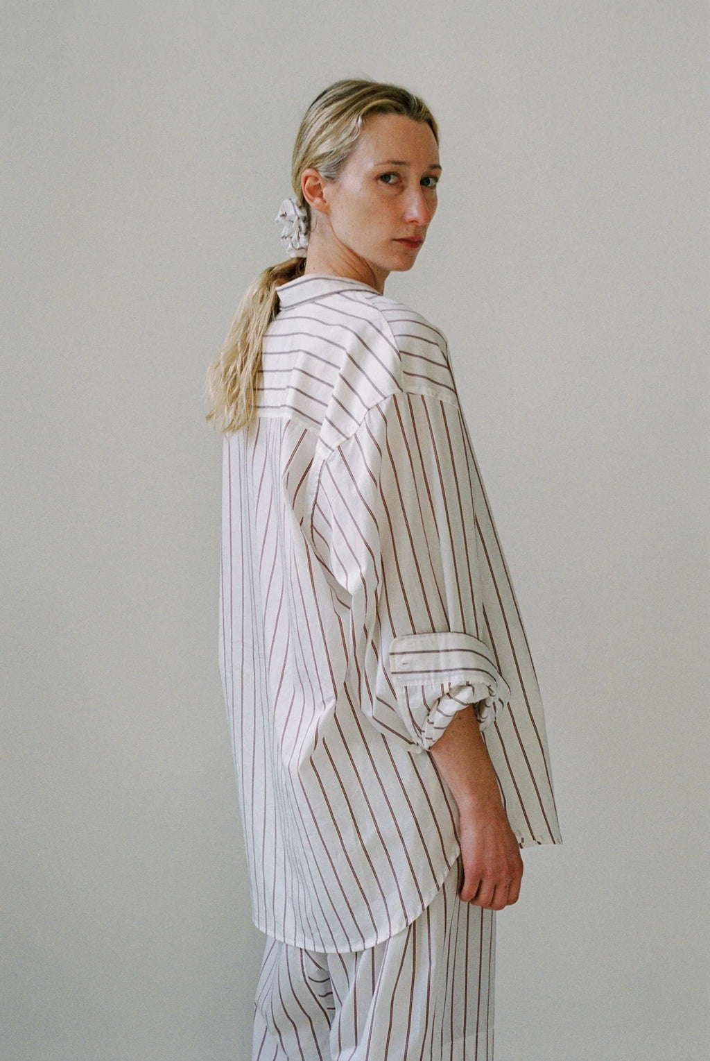 Woman wearing a white and gray striped outfit against a plain background