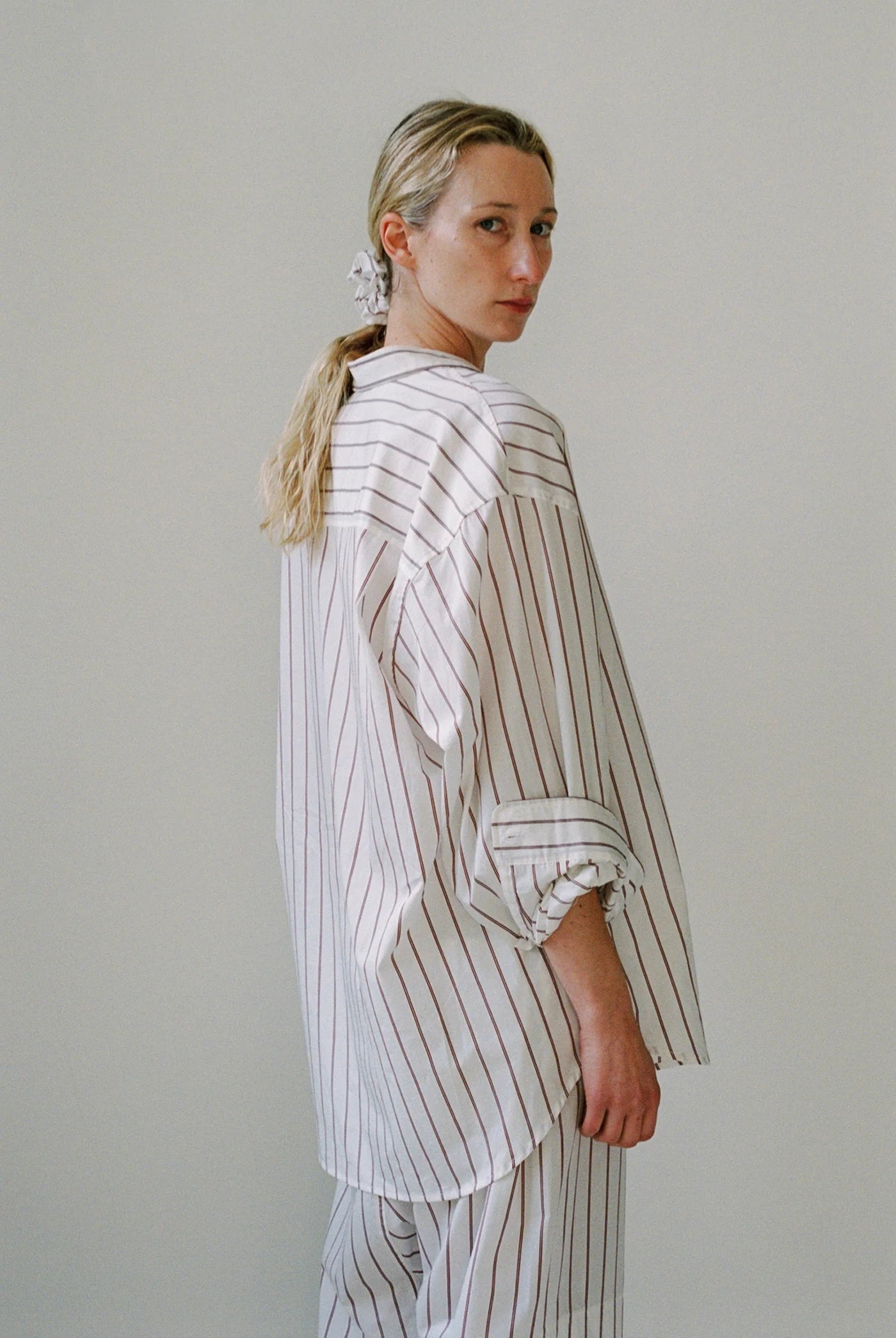 Woman wearing a white and gray striped outfit against a plain background