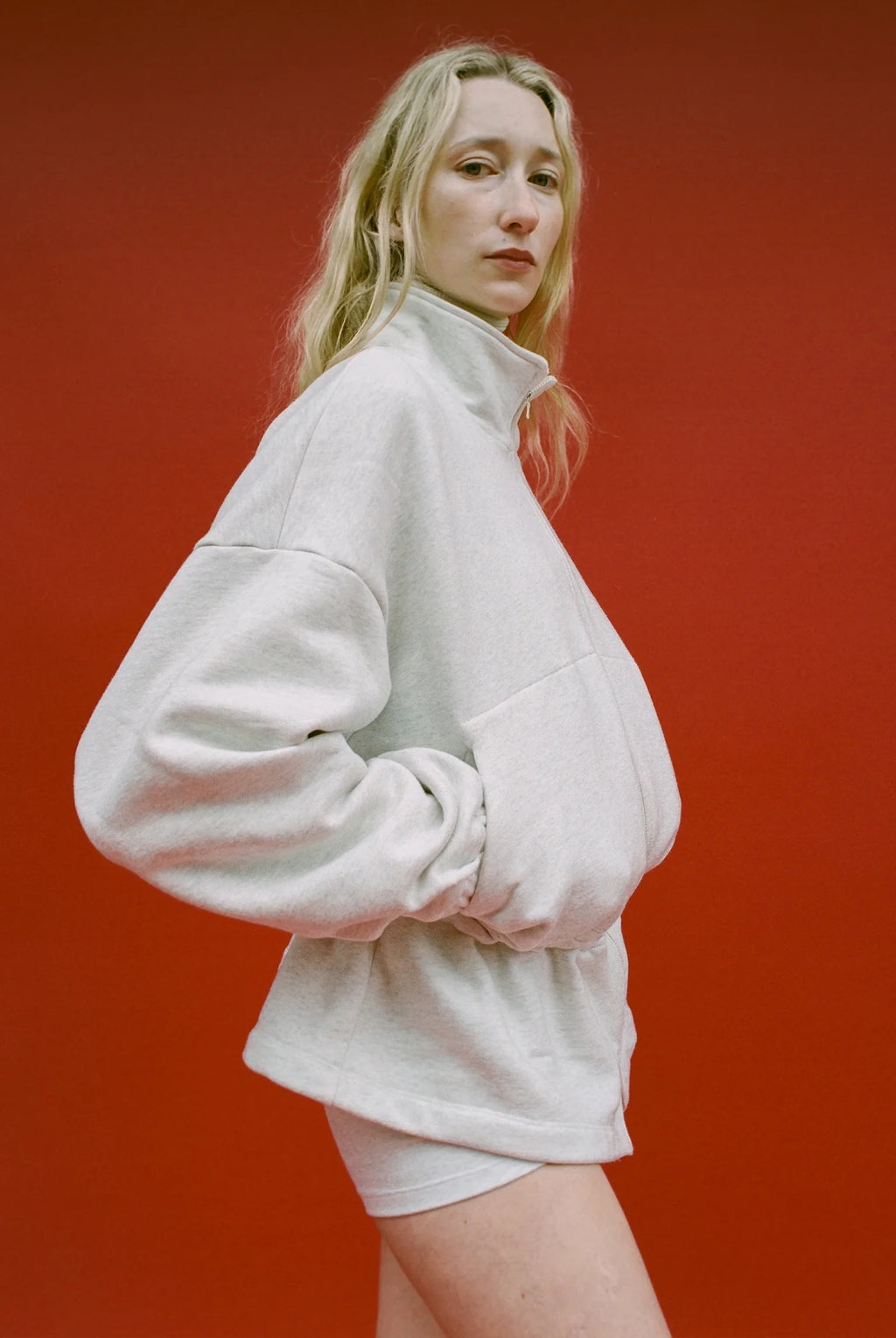 Woman wearing a light gray oversized sweatshirt and shorts against a red background