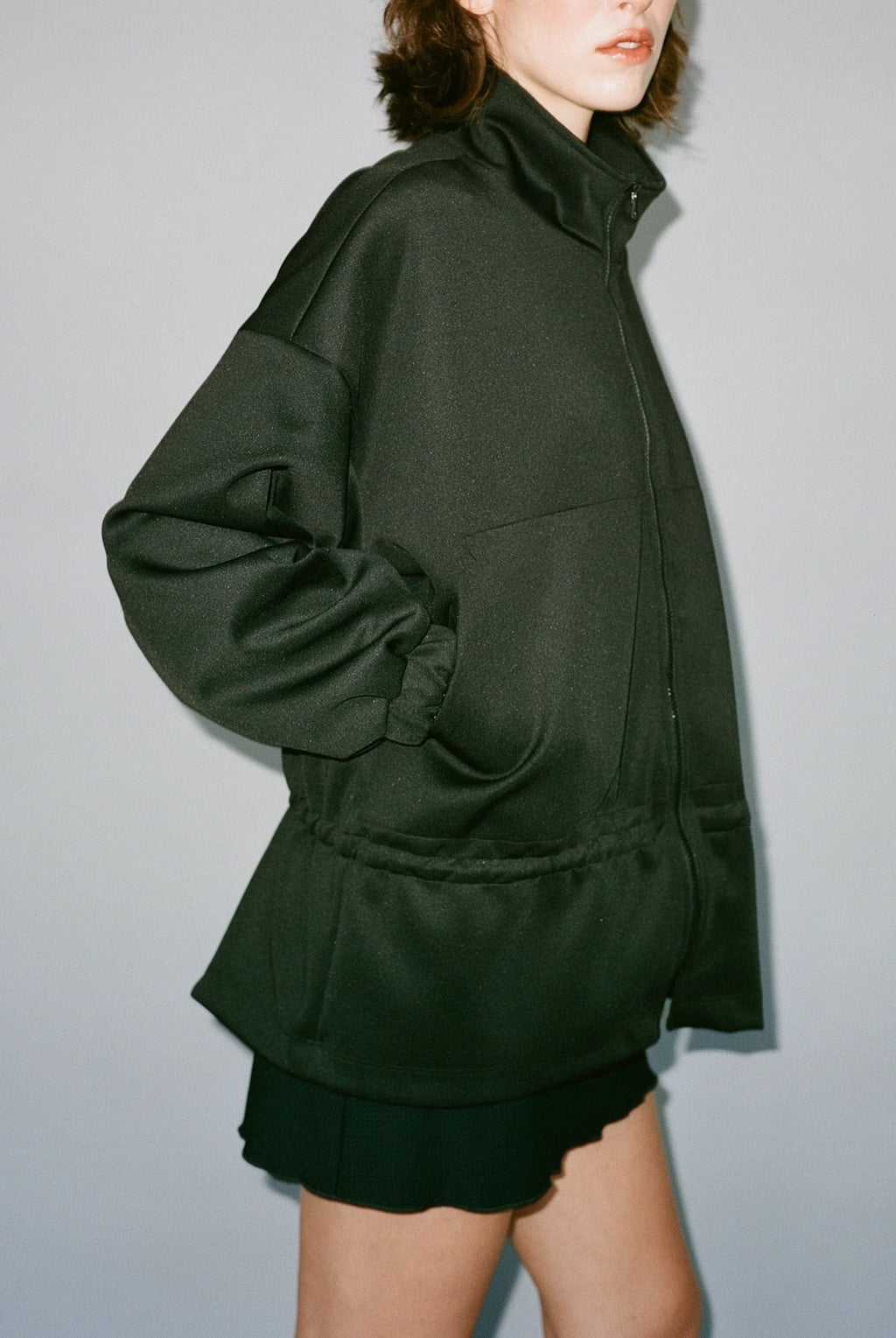 Person wearing a dark green jacket and skirt against a plain background