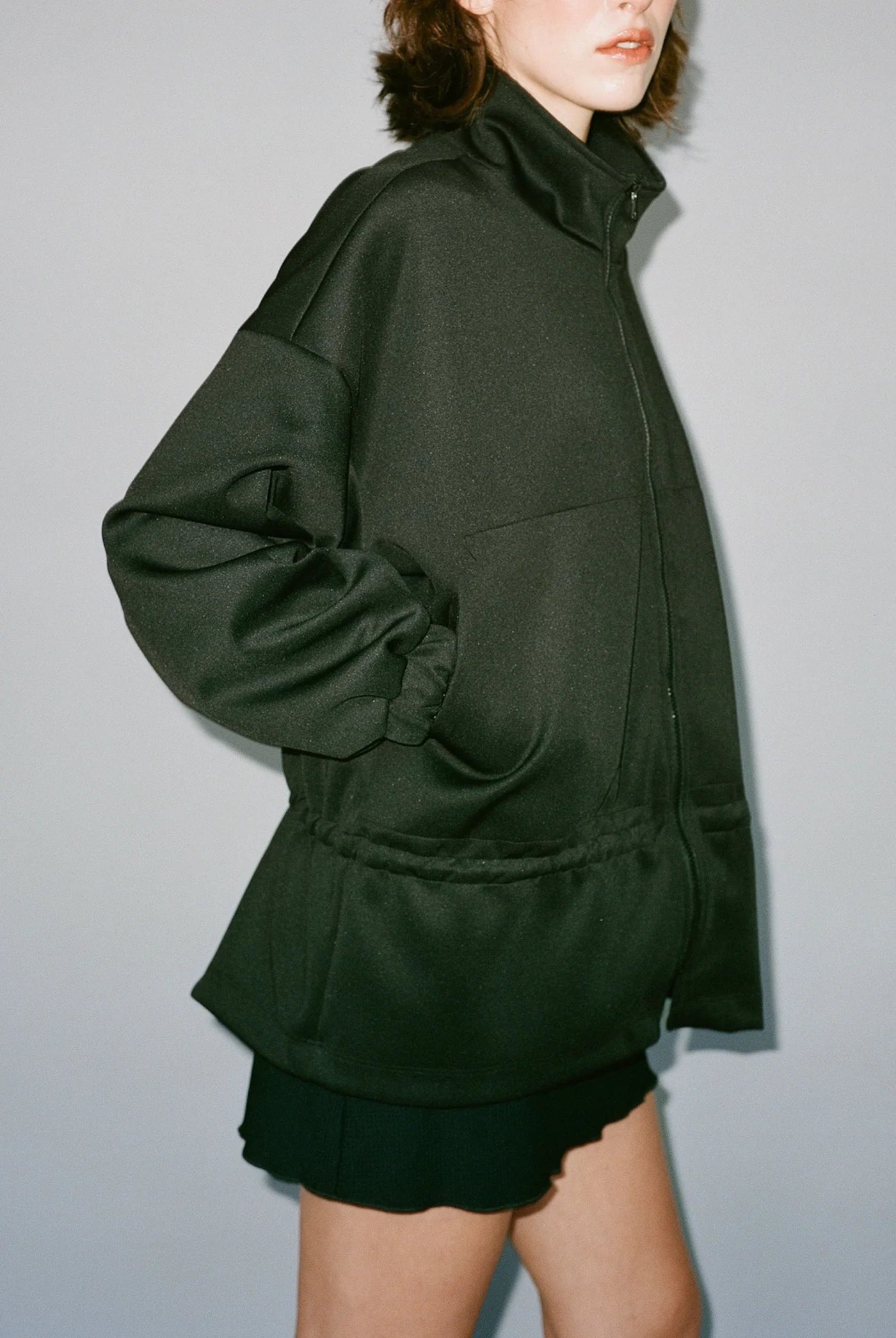 Person wearing a dark green jacket and skirt against a plain background