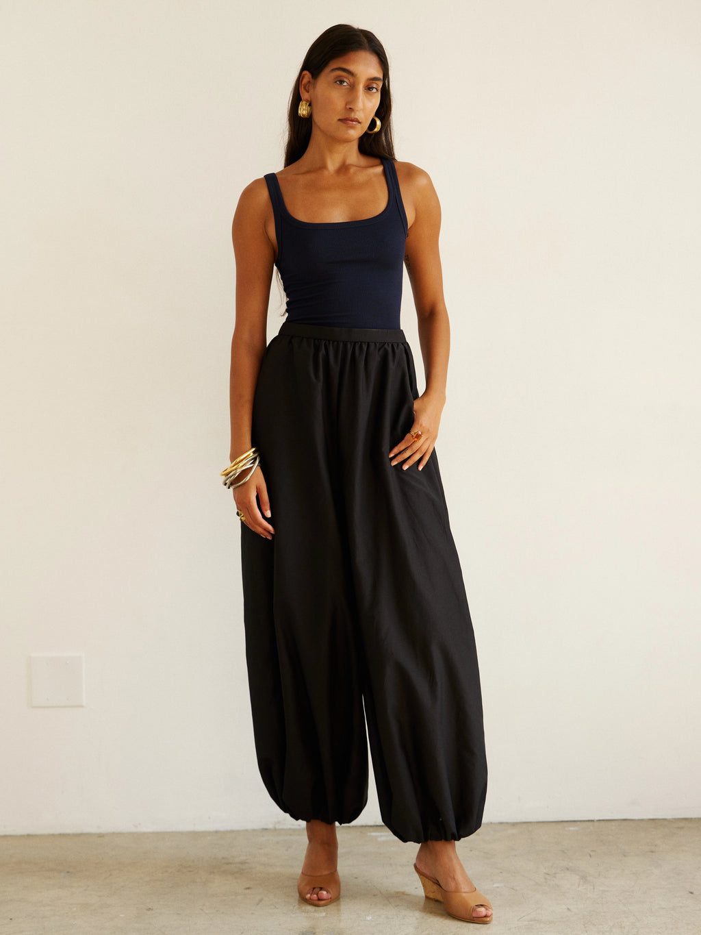 Woman wearing a black sleeveless top and wide-leg pants against a white background