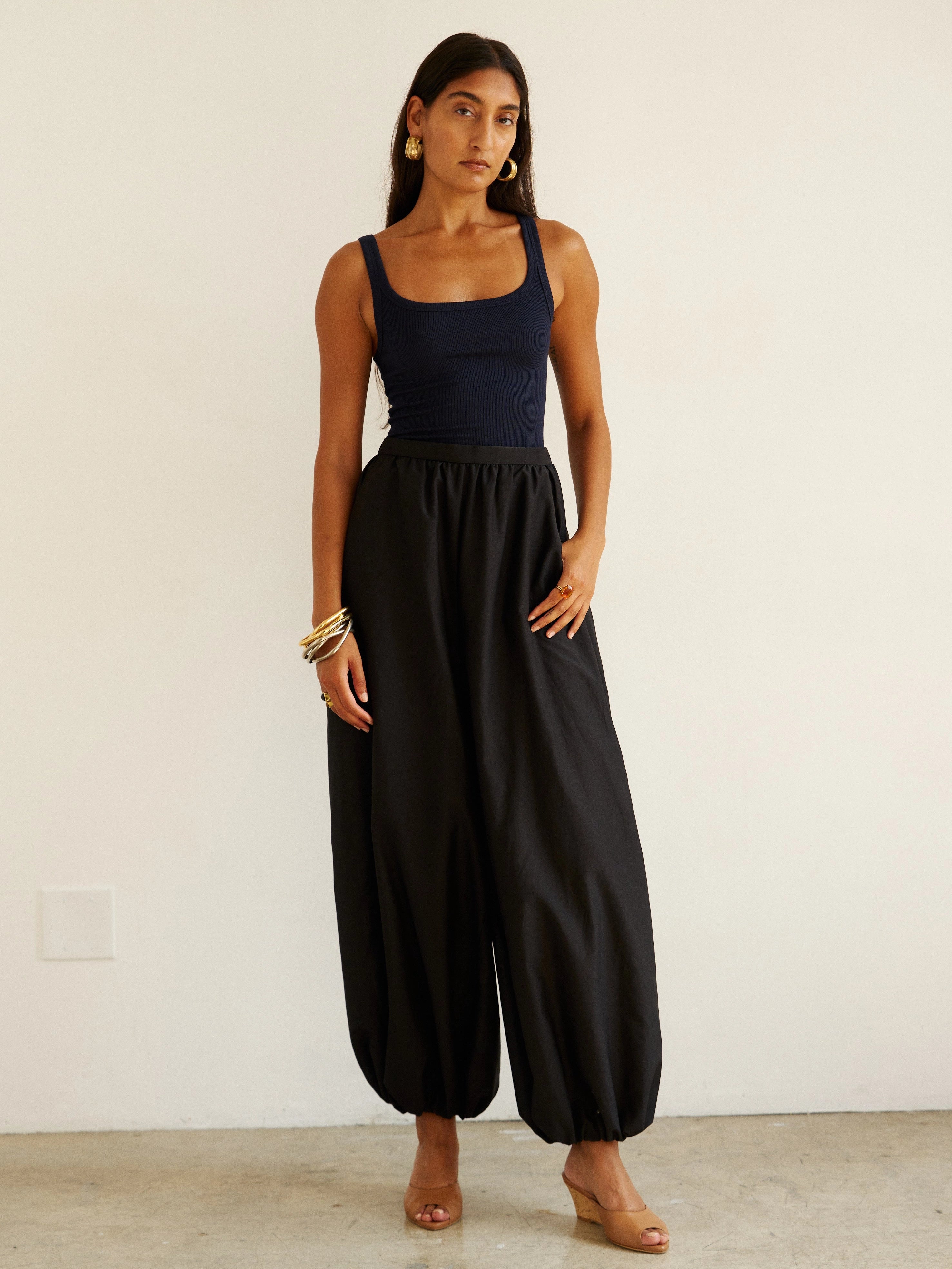 Woman wearing a black sleeveless top and wide-leg pants against a white background