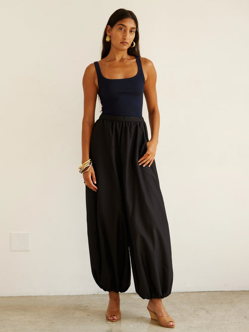 Woman wearing a black sleeveless top and wide-leg pants against a white background