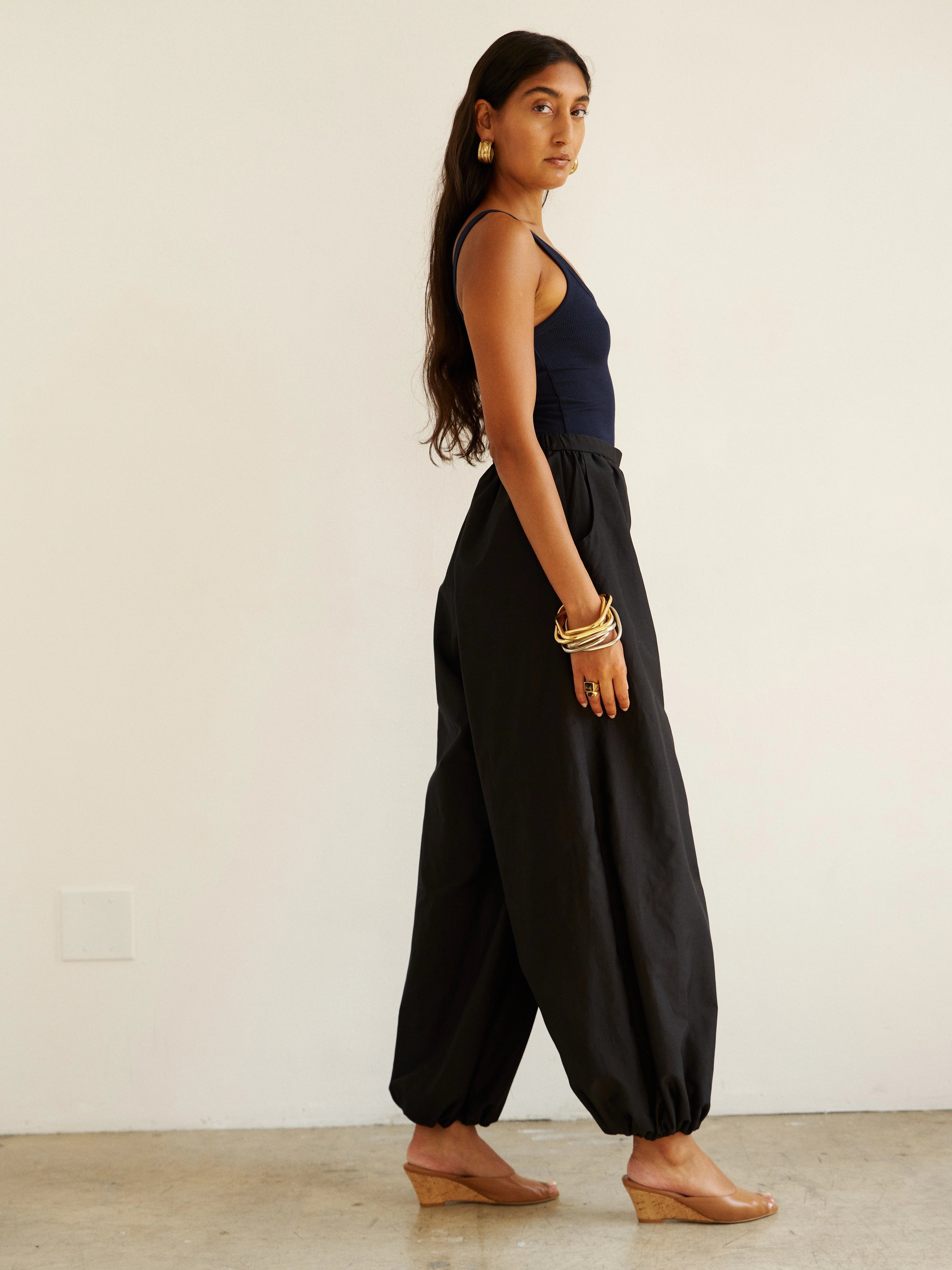 Woman wearing black wide-leg pants and a dark top against a white background