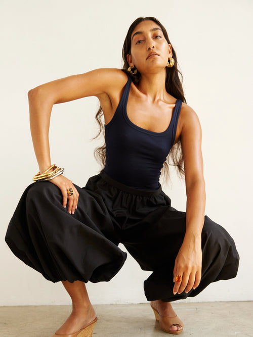 Woman wearing a navy tank top and black pants against a white background