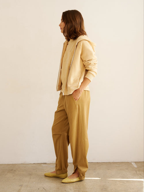 Person wearing a beige outfit standing against a white wall.