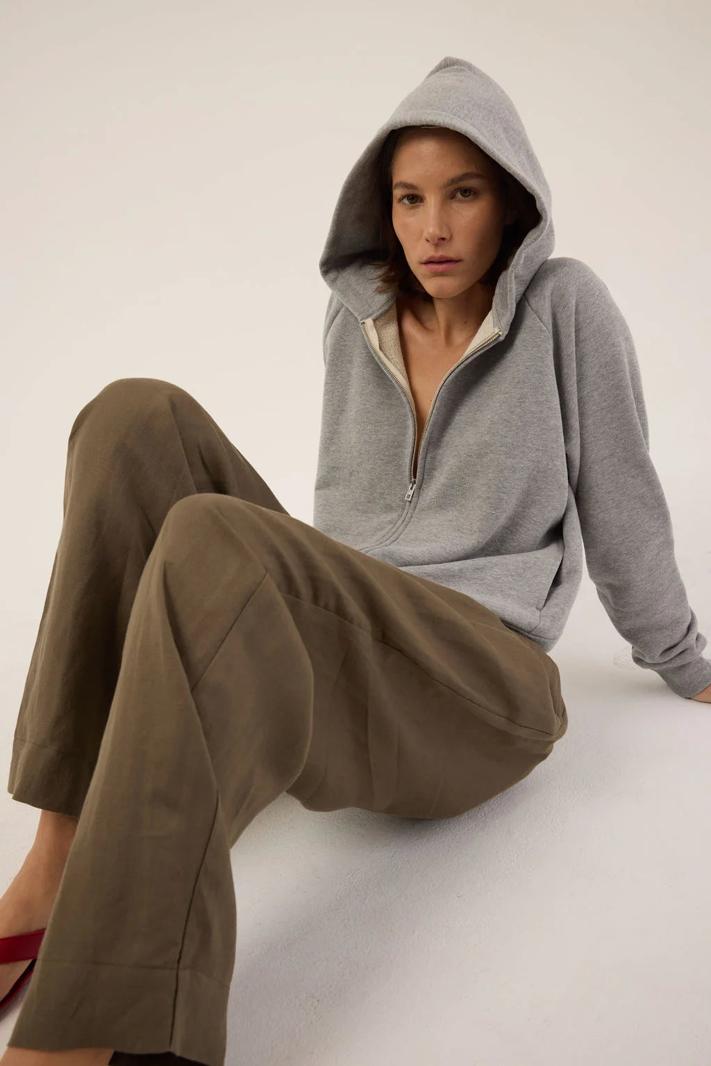 Person wearing a gray hoodie and brown pants sitting on a white surface.