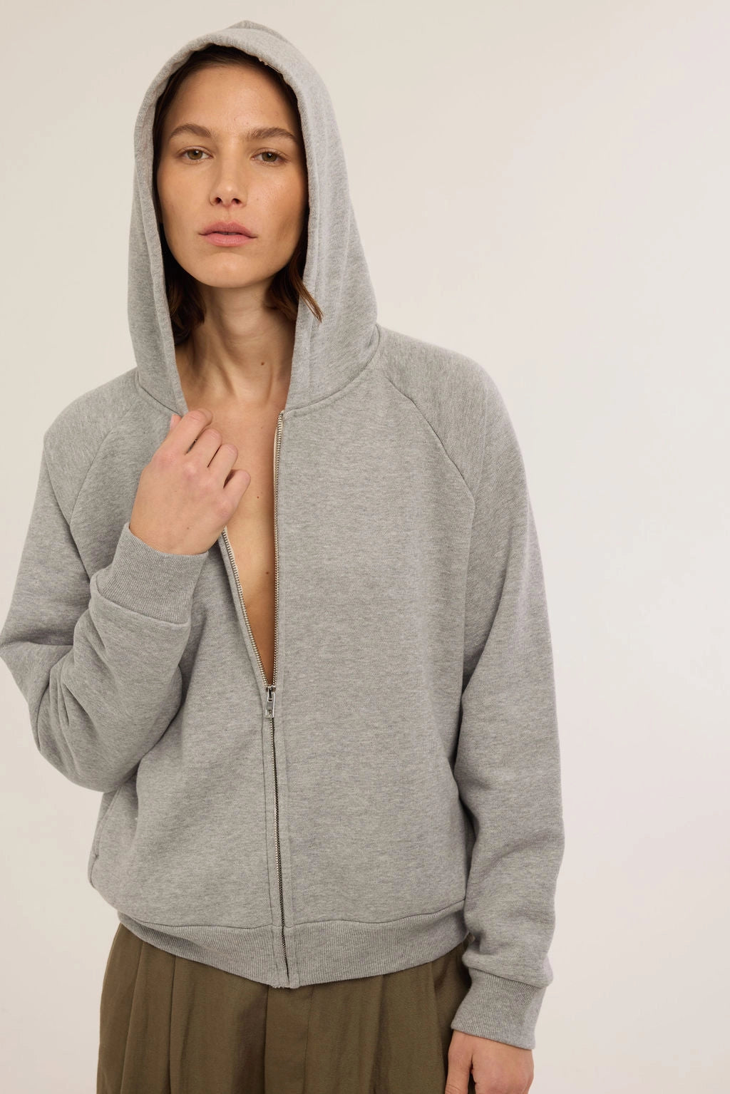 Person wearing a gray hoodie with the top button undone on a plain background