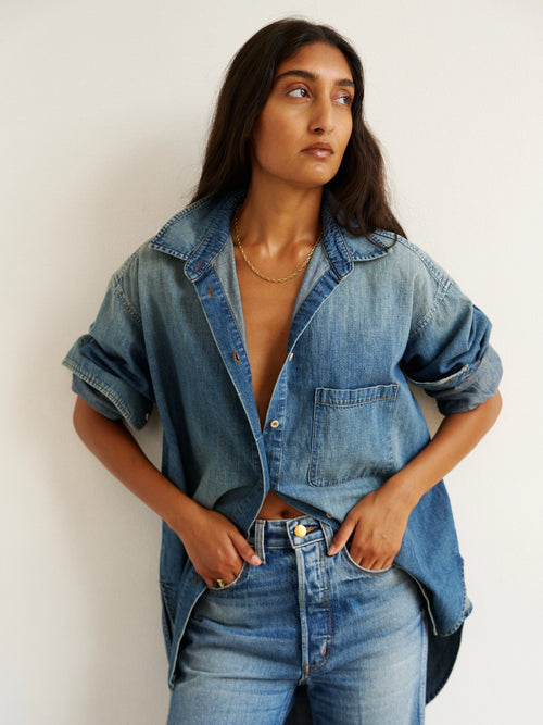 Woman wearing a denim shirt and jeans against a plain background