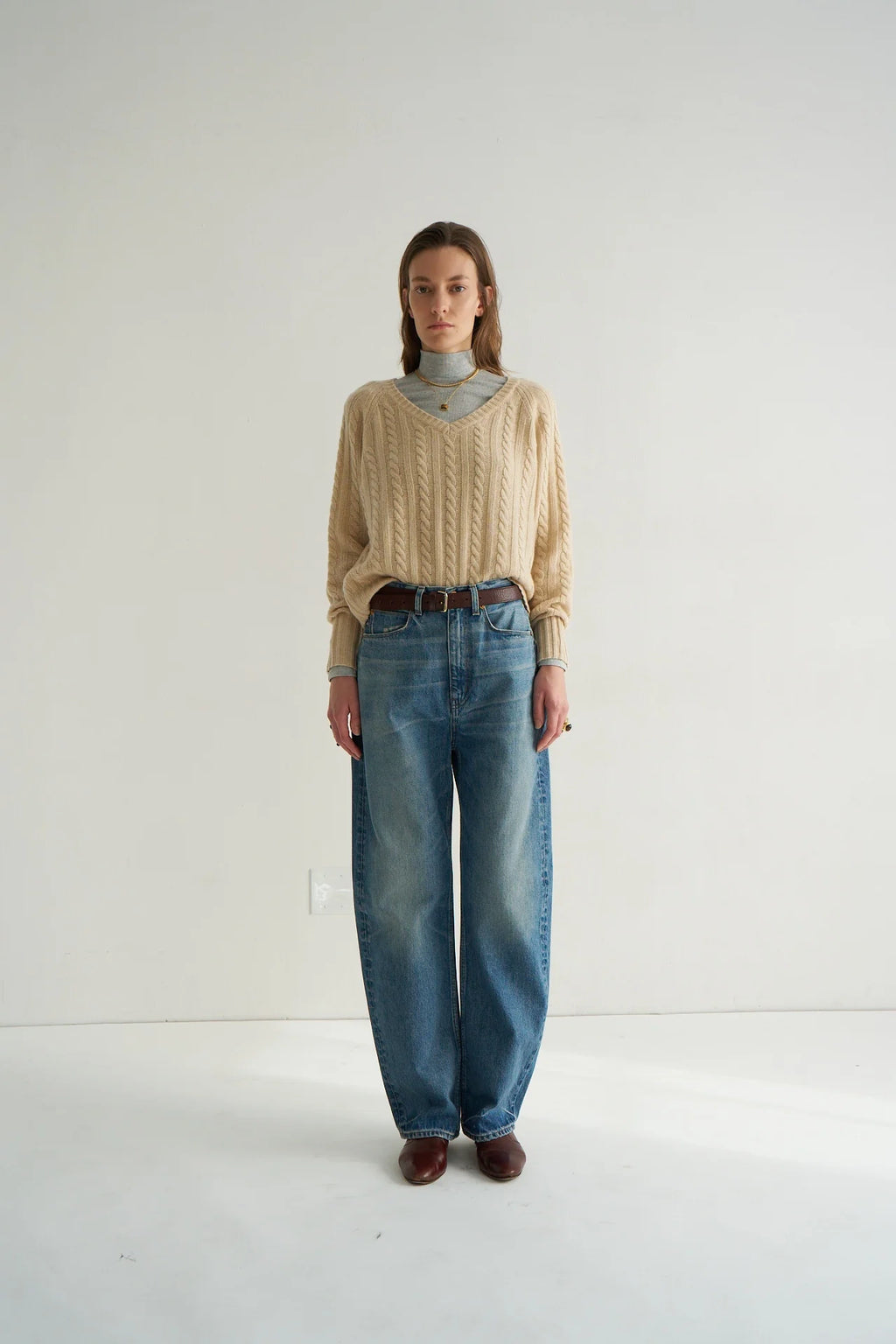 Person wearing a beige cable knit sweater and blue jeans on a white background