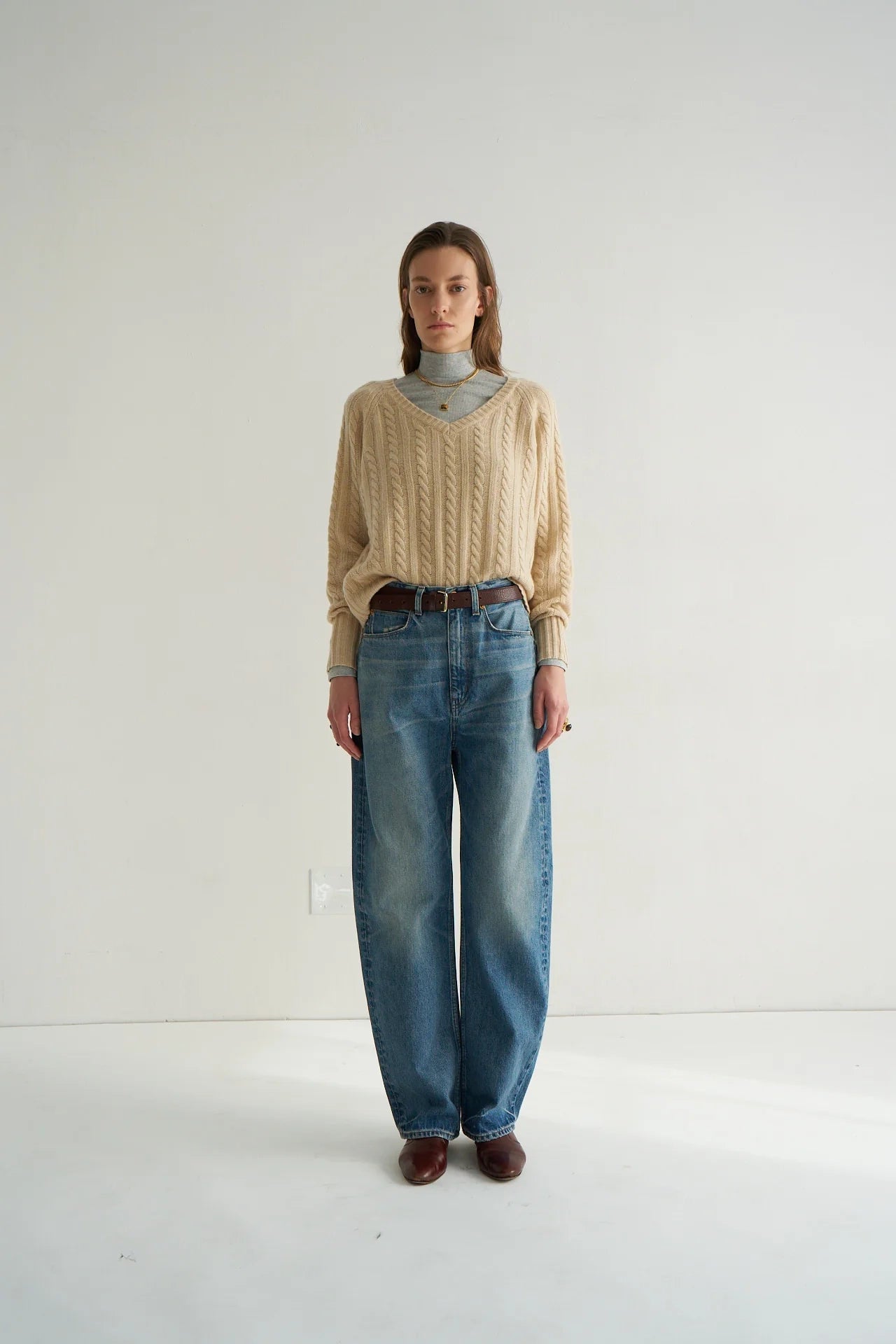 Person wearing a beige cable knit sweater and blue jeans on a white background