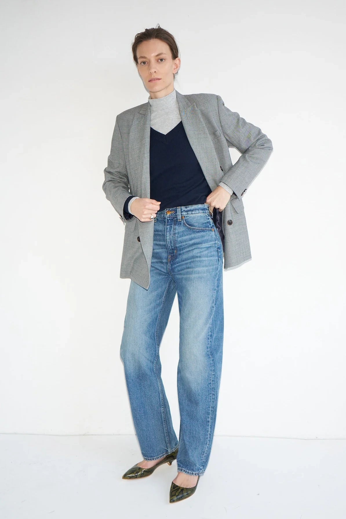 Person wearing a gray blazer, navy sweater, and blue jeans on a white background