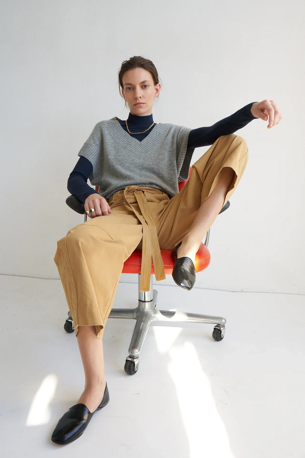 Person sitting on a chair wearing a gray sweater, black shirt, tan pants, and black shoes.