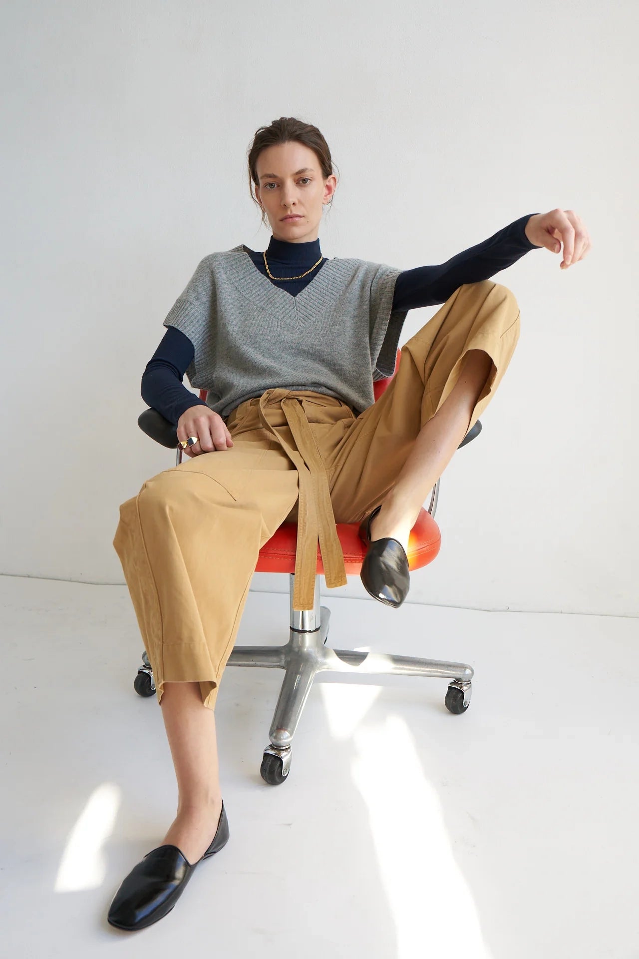 Person sitting on a chair wearing a gray sweater, black shirt, tan pants, and black shoes.