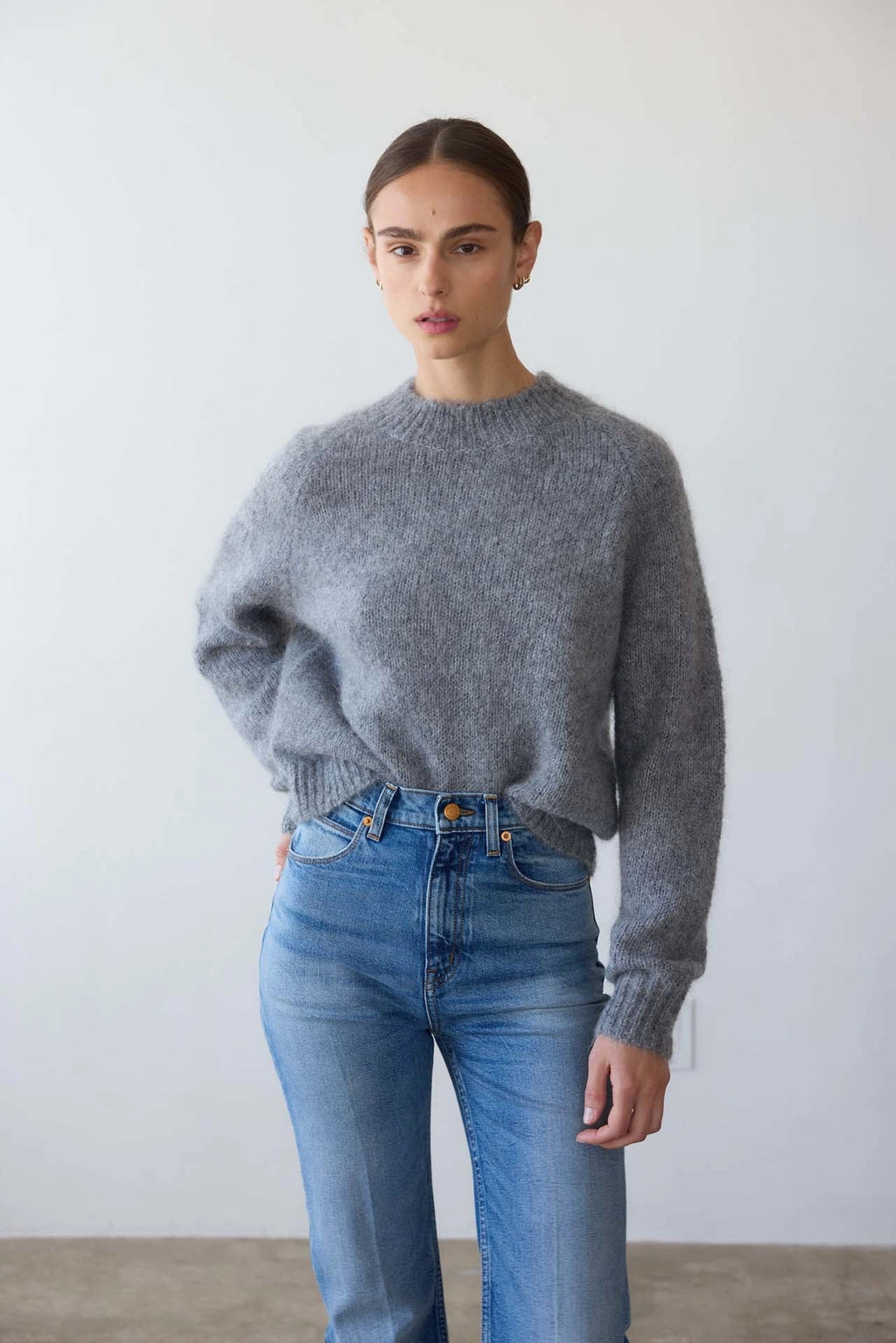 Person wearing a gray sweater and blue jeans against a plain background