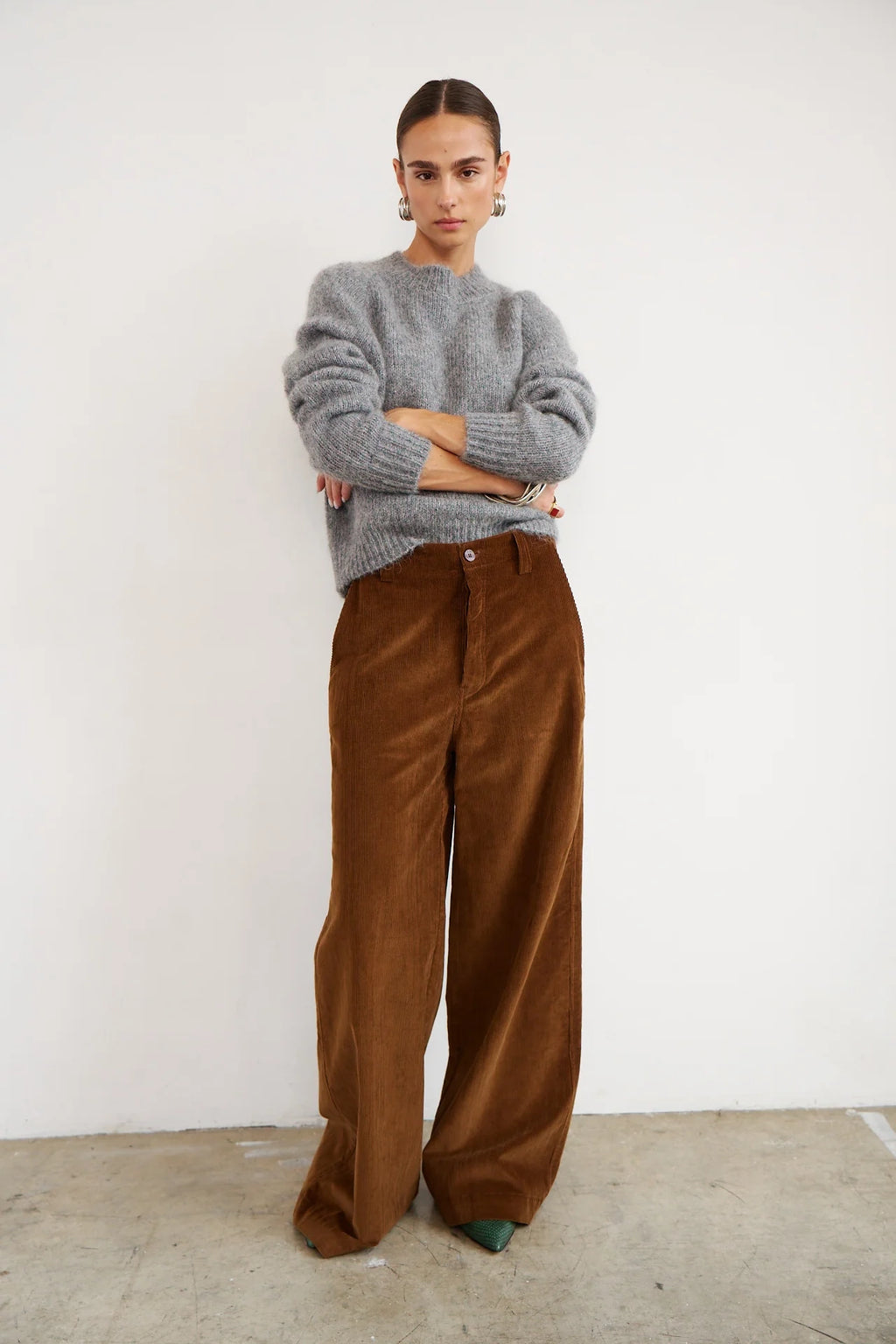 Person wearing a gray sweater and brown pants against a white background