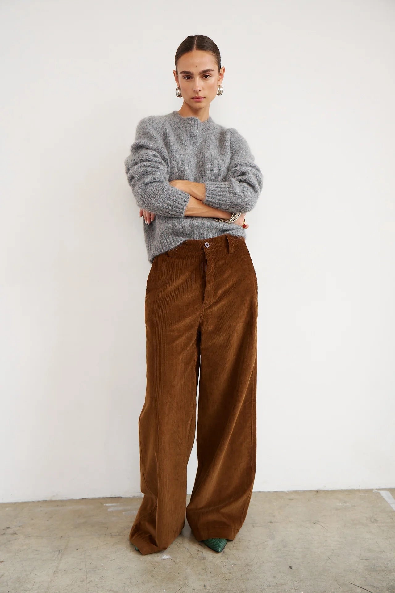 Person wearing a gray sweater and brown pants against a white background