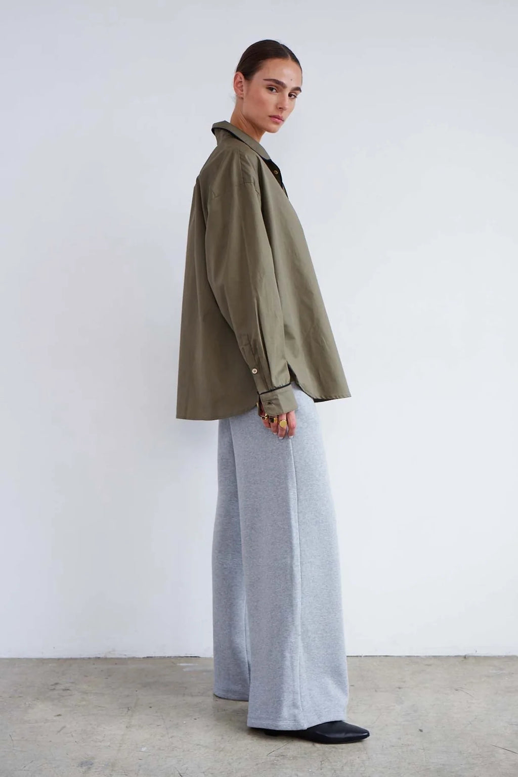 Person wearing a green jacket and light gray pants against a white background