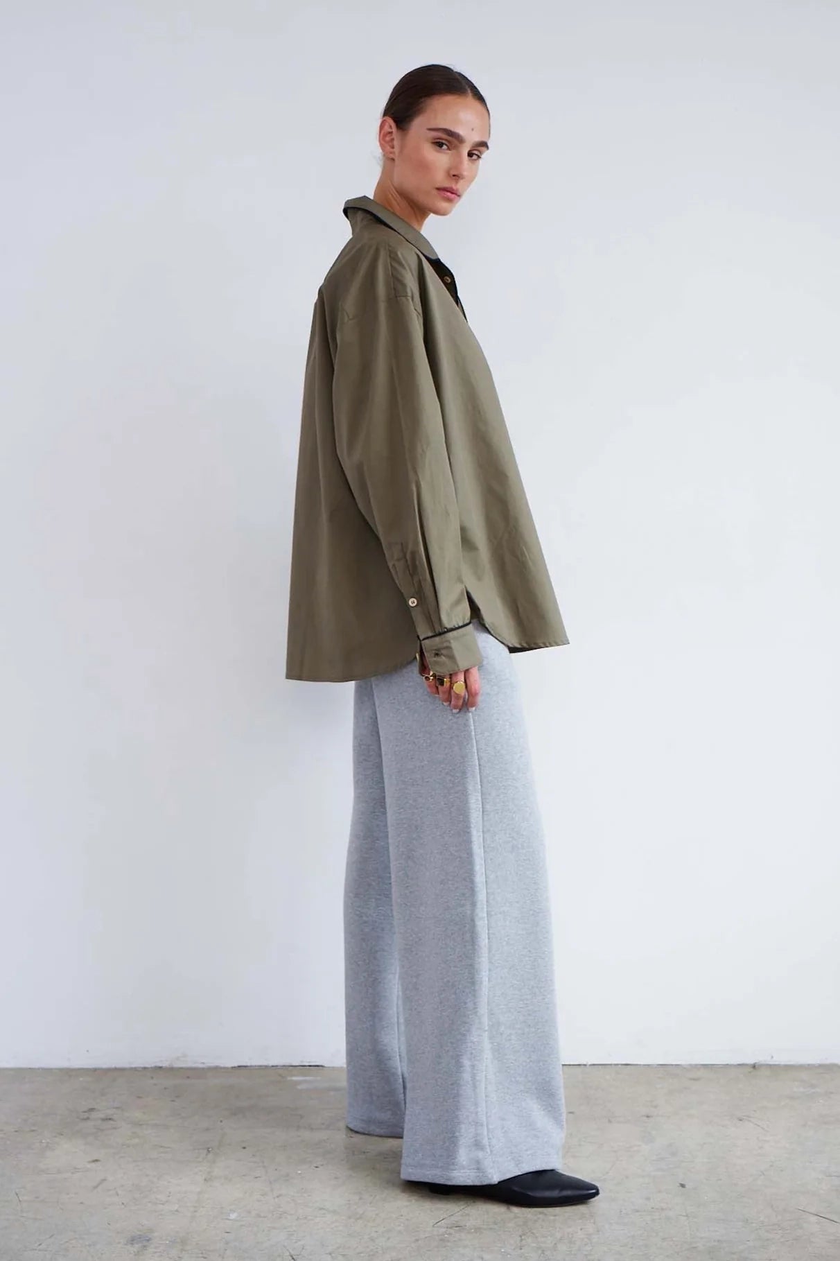 Person wearing a green jacket and light gray pants against a white background