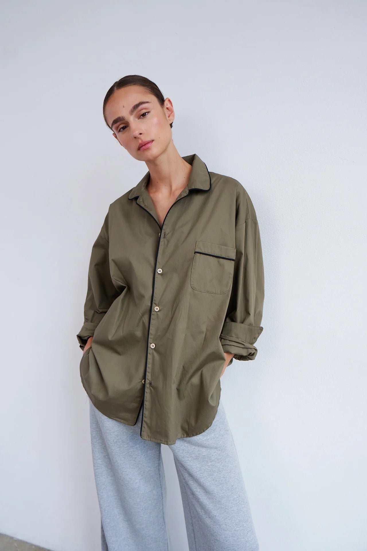 Person wearing an olive green shirt with a plain background