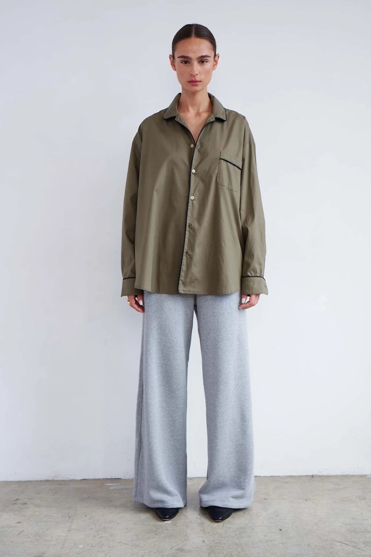 Person wearing an olive green shirt and light gray pants against a white background