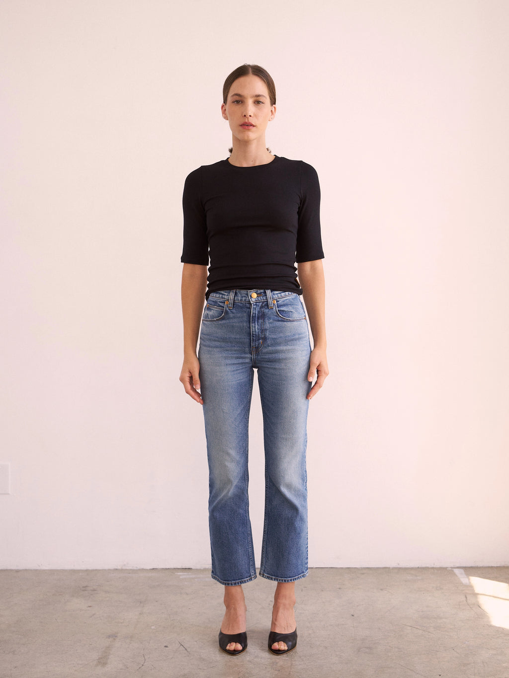Woman wearing a black top and blue jeans against a white background