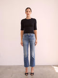 Woman wearing a black top and blue jeans against a white background