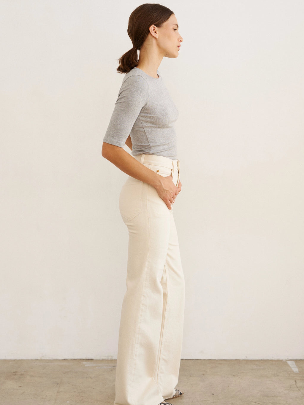 Woman wearing a gray top and white pants against a plain background