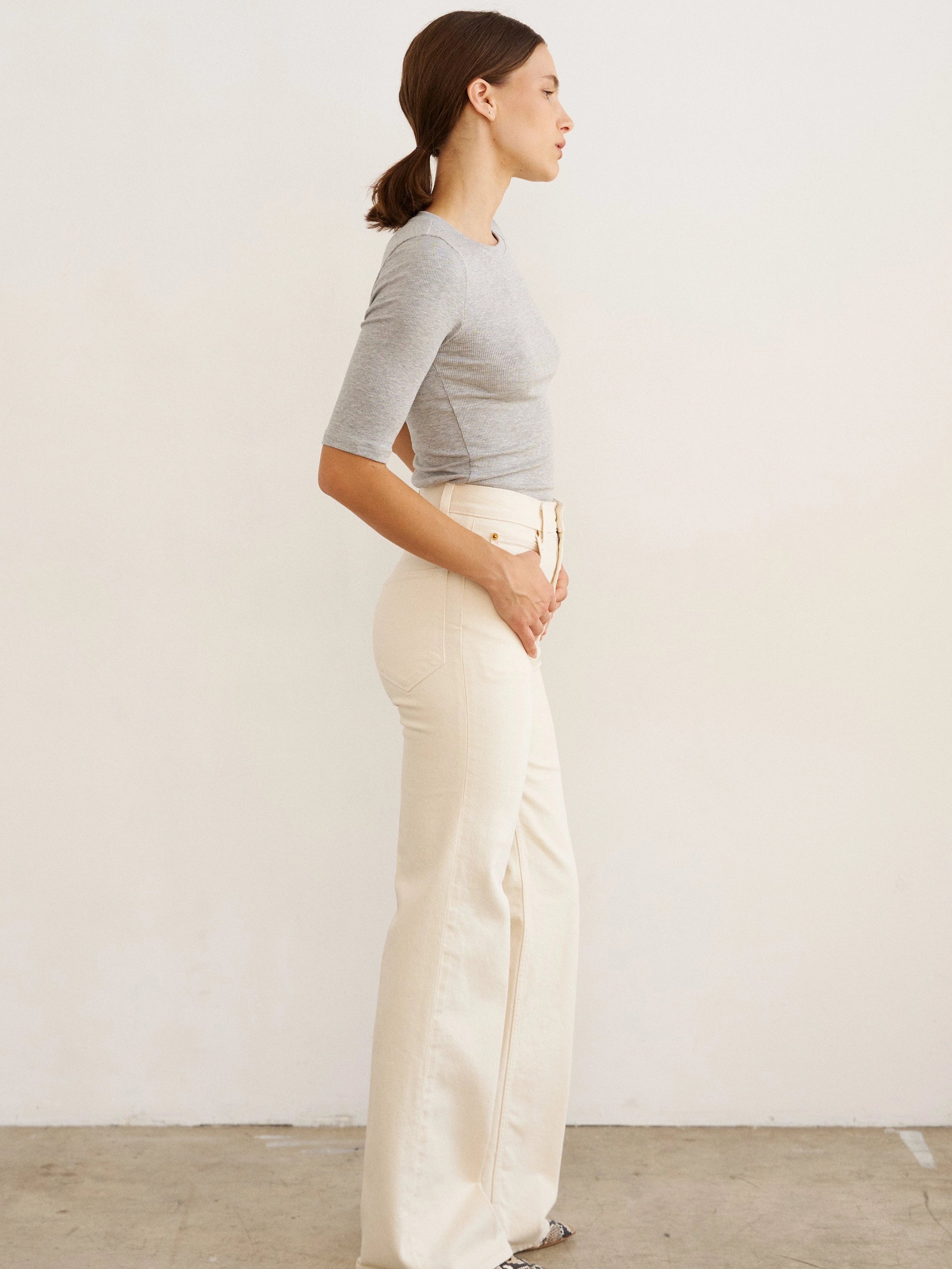 Woman wearing a gray top and white pants against a plain background