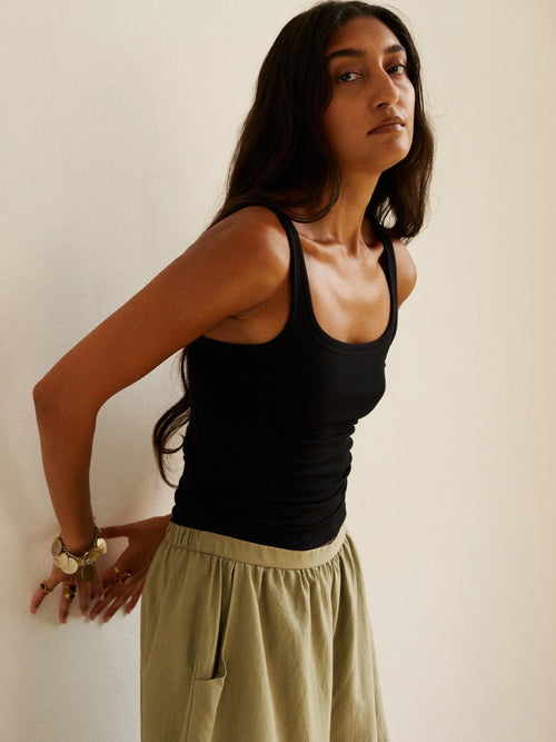 Woman wearing a black tank top and beige pants against a plain background