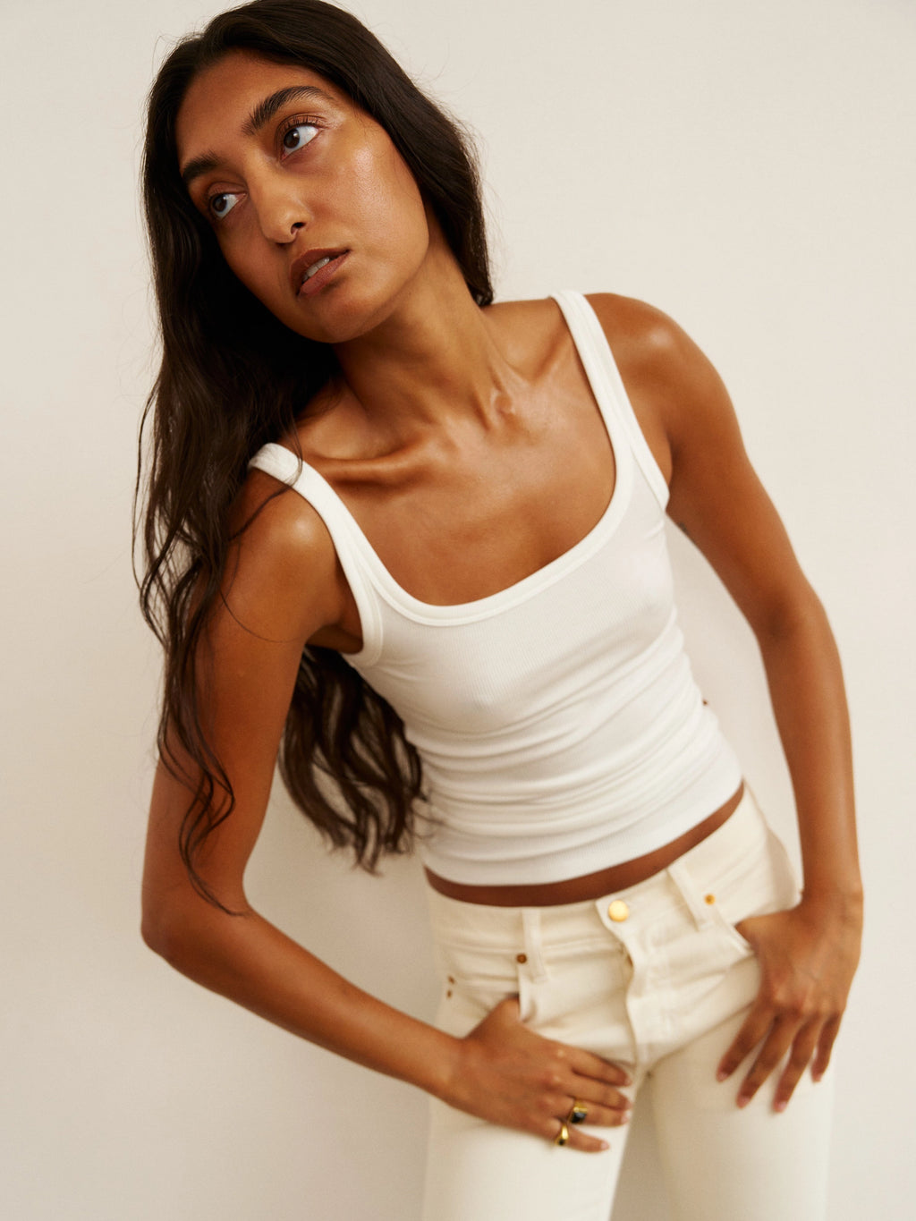Woman wearing a white tank top and pants against a plain background