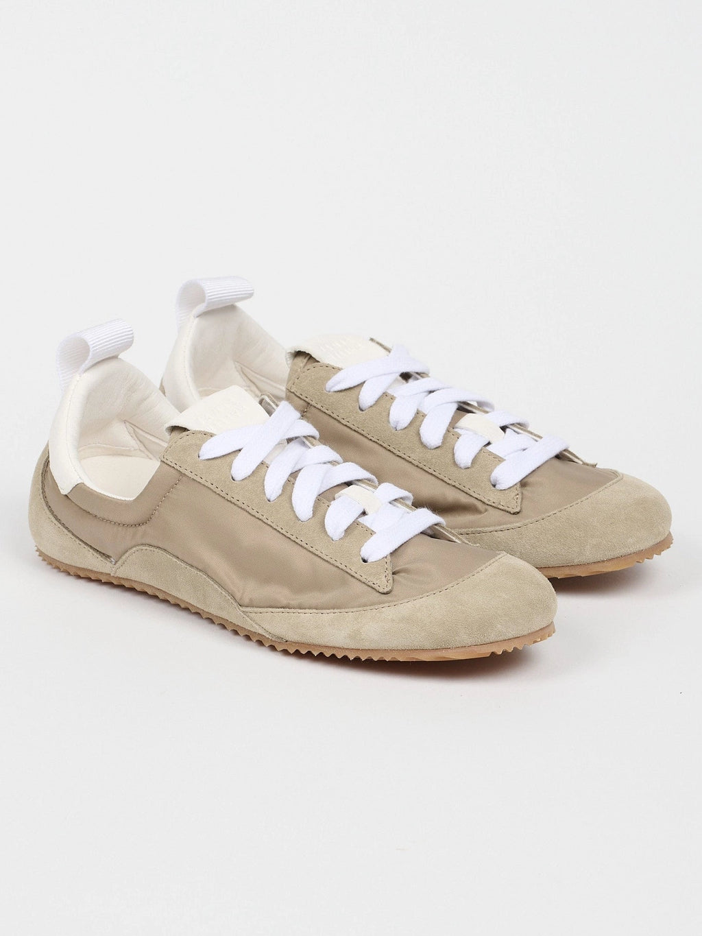 Pair of beige sneakers with white laces on a light gray background