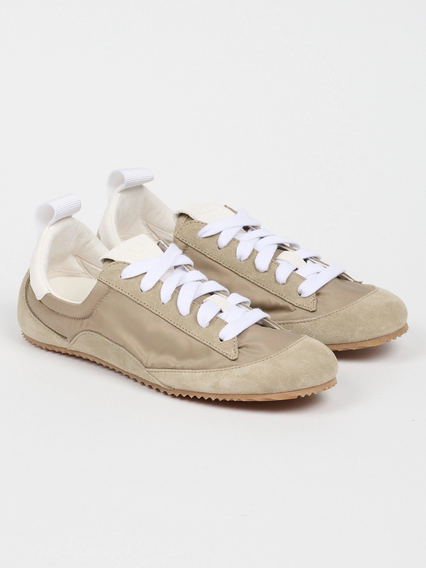Pair of beige sneakers with white laces on a light gray background