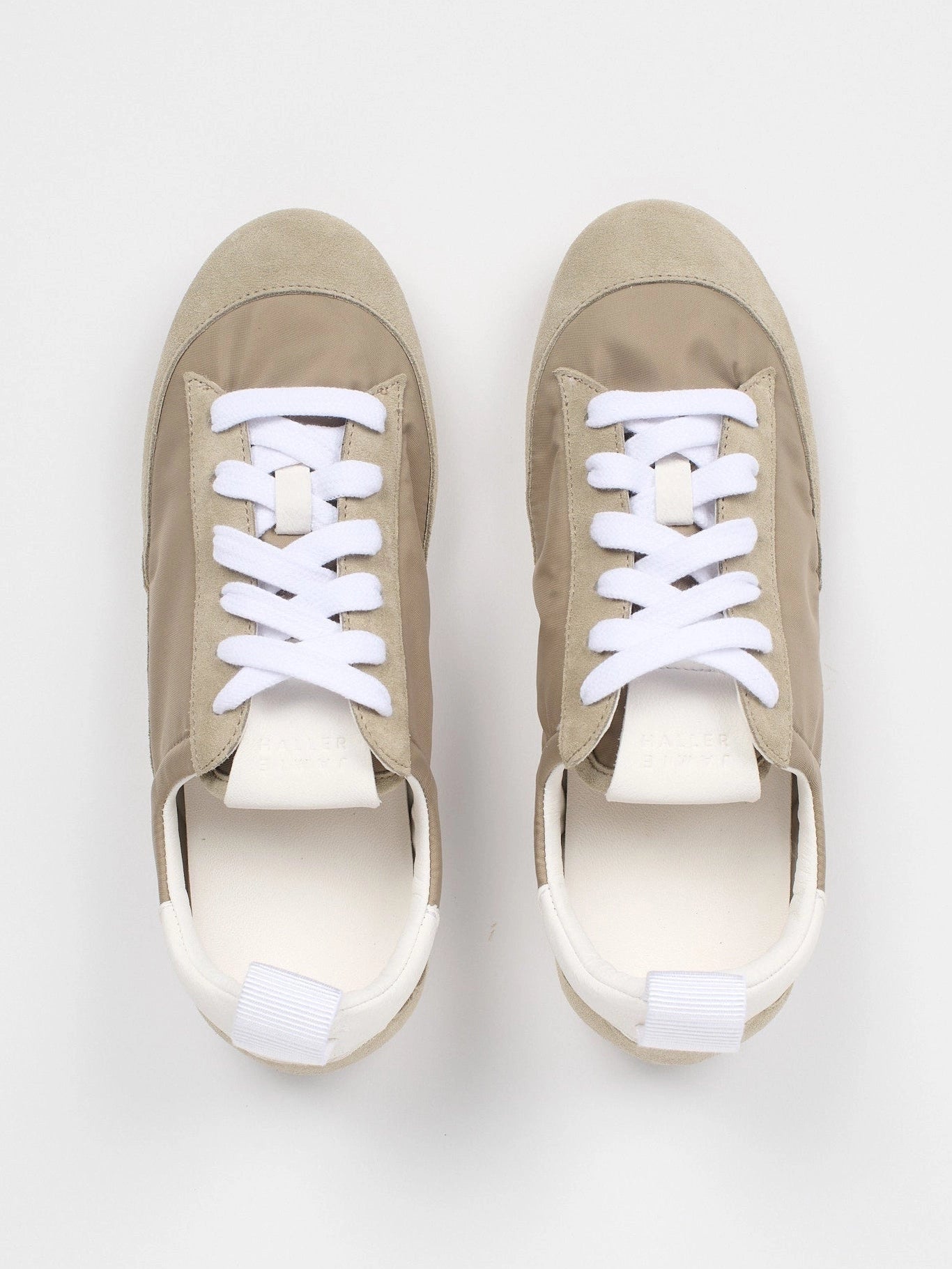 Pair of beige sneakers with white laces on a light gray background