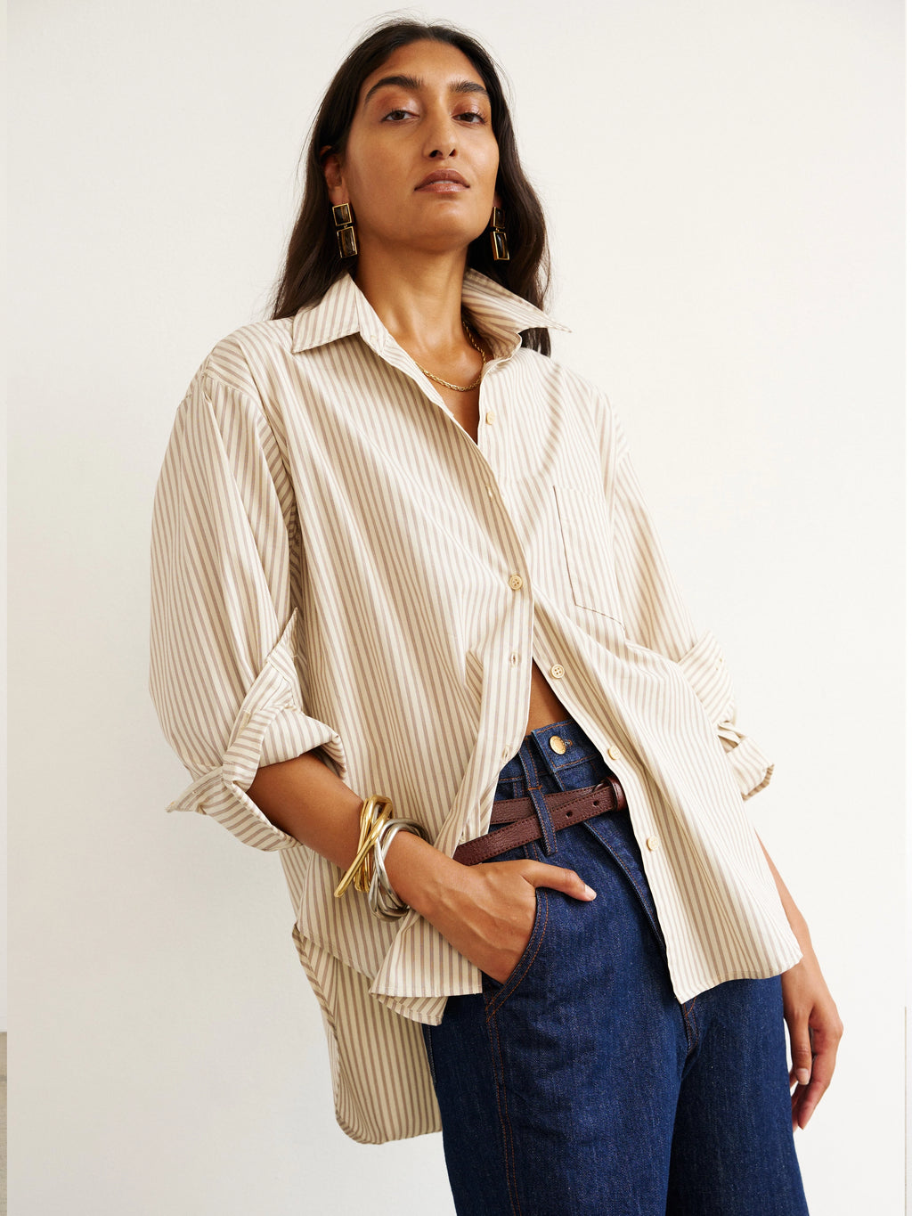 Woman wearing a beige striped shirt and blue jeans against a white background