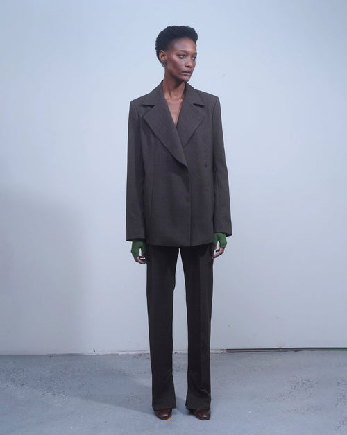 Model wearing NOMIA Double Breasted Jacket in earth with a structured silhouette, side slits and waist carabiner detail.