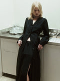 NOMIA duster coat in black with a straight, elongated silhouette, button front and back vent, worn over a matching skirt.