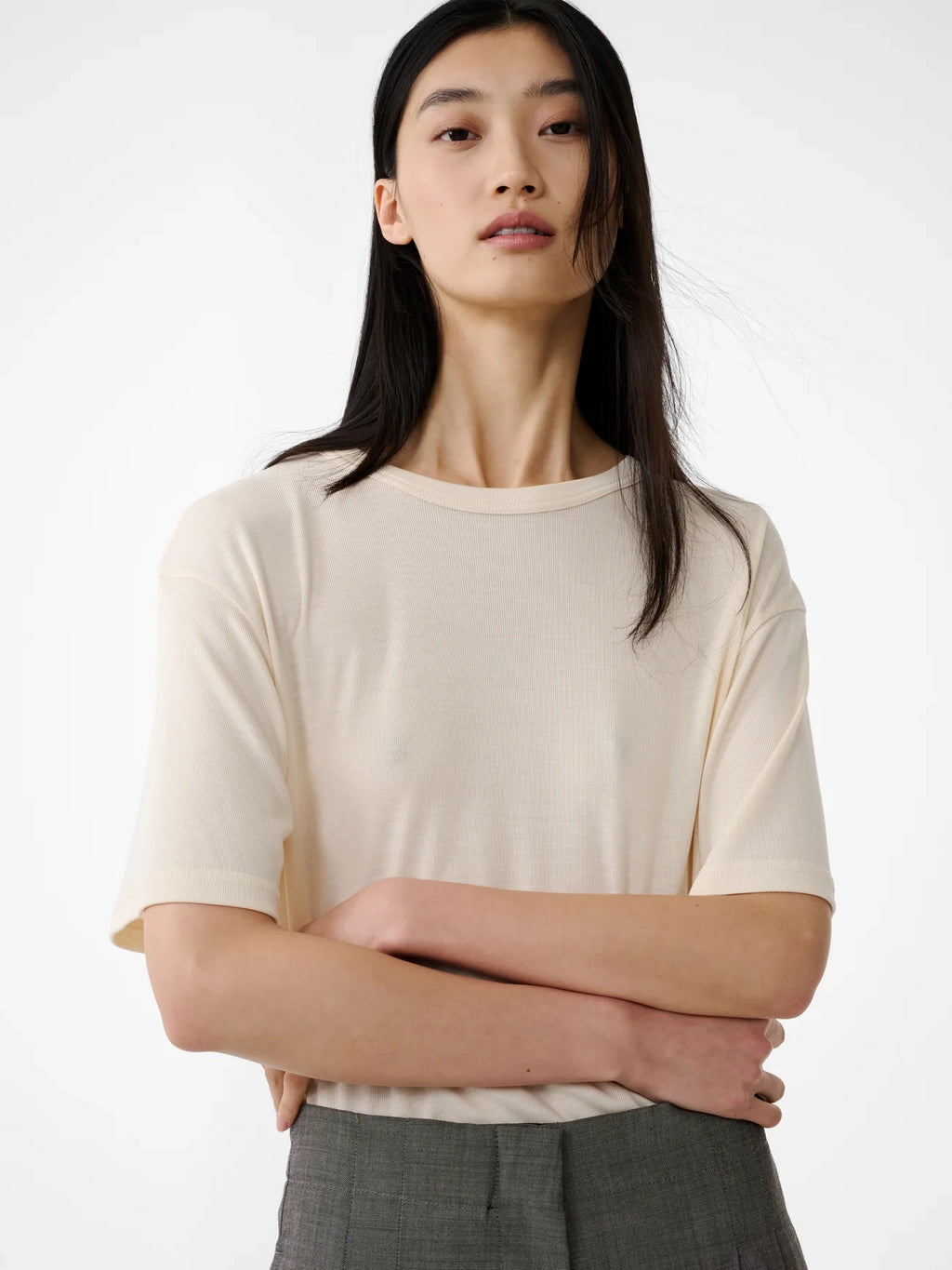 Person wearing a beige top with crossed arms on a white background